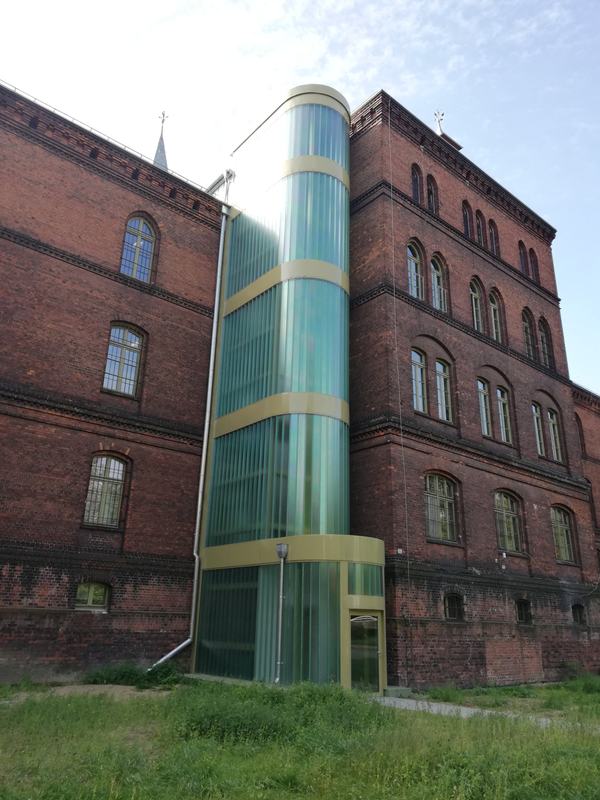 Owalny szyb windy z profilowanego szkła przy ceglanym budynku